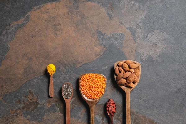 Tendido plano de cucharas de madera arregladas con superalimentos, lentejas rojas y cúrcuma en la mesa con espacio para copiar - foto de stock