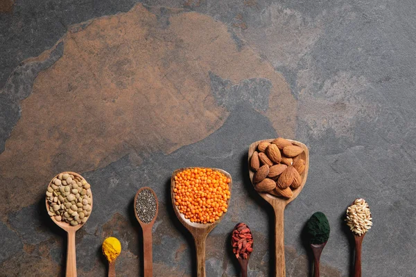 Vista dall'alto di cucchiai di legno disposti con superalimenti e fagioli sul tavolo con spazio copia — Foto stock