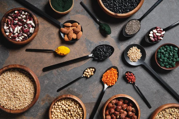 Vista dall'alto di ciotole e cucchiai in legno con superalimenti, legumi e cereali sul tavolo — Foto stock