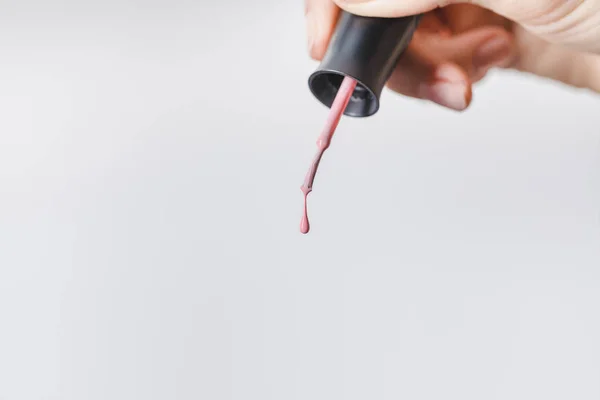 Vista recortada de mujer sosteniendo cepillo con esmalte de uñas rosa aislado en gris - foto de stock