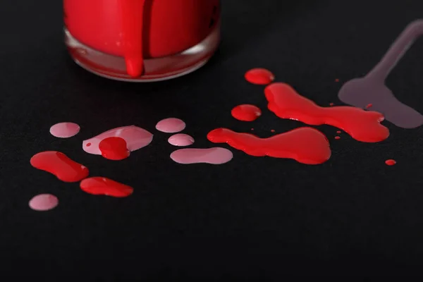 Vista de cerca de la botella de esmalte de uñas con gotas rojas y rosadas aisladas en negro - foto de stock
