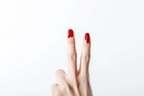 Vista recortada de la mujer que muestra signo de paz con esmalte de uñas rojo goteo aislado en gris - foto de stock