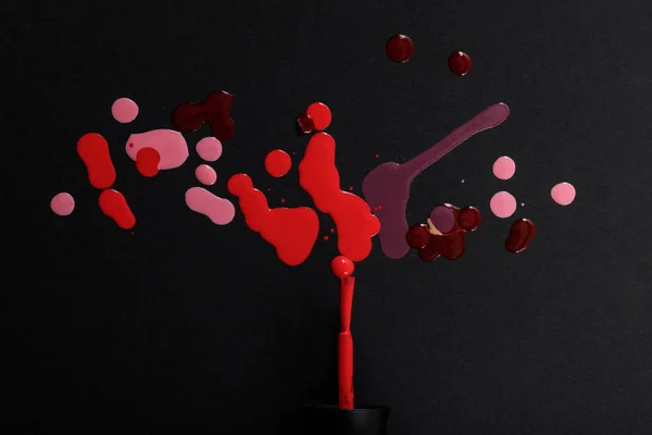 Ansicht von Nagellackpinsel mit bunten roten, weinroten und rosa Tropfen isoliert auf schwarz — Stockfoto