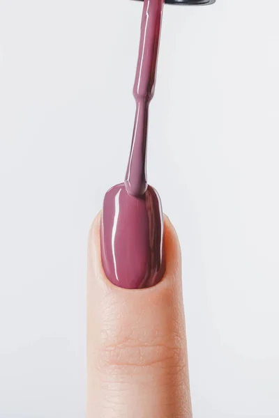 Abgeschnittene Ansicht einer Frau, die lila Pastelllack auf den Fingernagel aufträgt, isoliert auf grau — Stockfoto