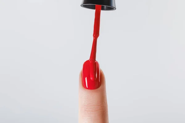 Vista recortada de la mujer aplicando esmalte de uñas rojo en la uña aislada en gris - foto de stock