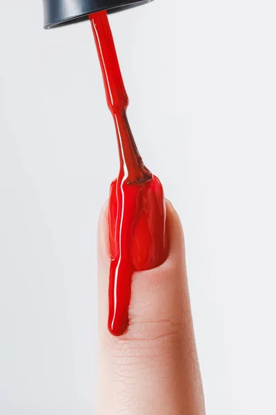 Vue partielle de la femme appliquant un vernis à ongles rouge dégoulinant sur l'ongle isolé sur gris — Photo de stock