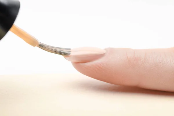 Esmalte de uñas de marfil en la uña de la mujer con cepillo húmedo sobre fondo blanco - foto de stock