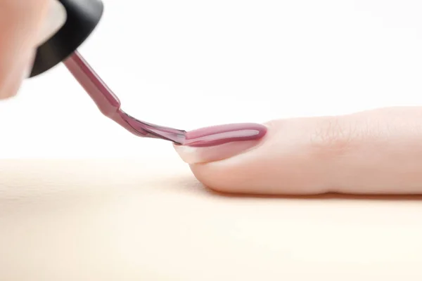 Manicurist applying purple nail polish on fingernail of woman on white background — Stock Photo