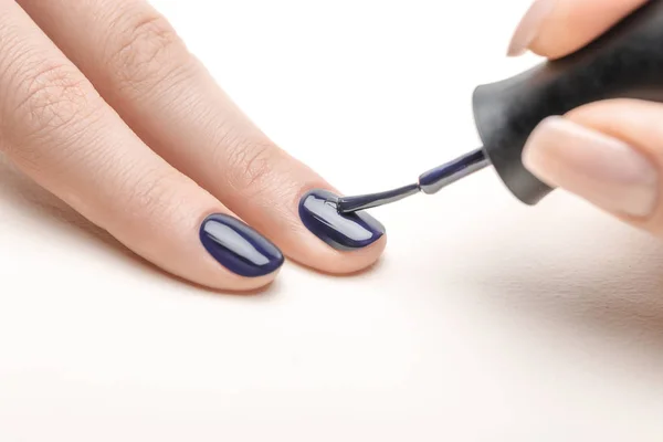 Female manicurist applying navy blue nail polish on fingernail of woman on white background — Stock Photo