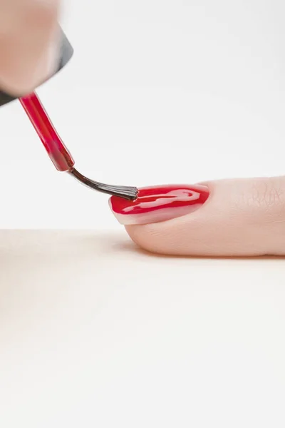 Manicurist applying bright red nail polish on fingernail of woman on grey background — Stock Photo