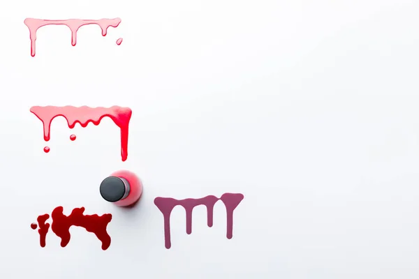 Top view of bottle with red nail polish near dripping multicolored spills isolated on grey — Stock Photo