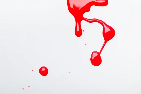 Top view of shiny red spilled nail polish with drops isolated on grey — Stock Photo