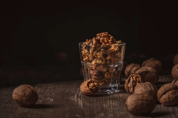 Close up view of shelled walnuts in glass on wooden tabletop on black background — Stock Photo