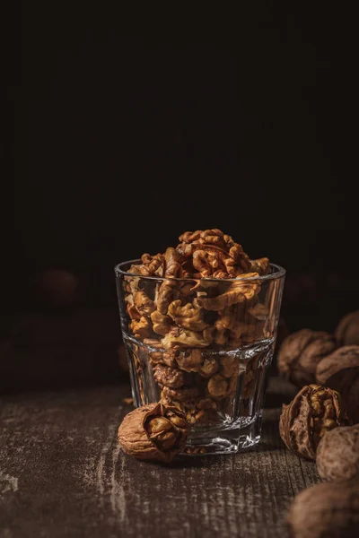 Close up view of shelled walnuts in glass on wooden tabletop on black background — Stock Photo