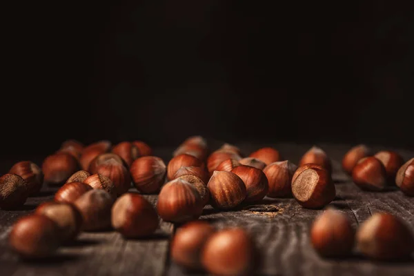 Close up view of hazelnuts on wooden surface on black background — Stock Photo