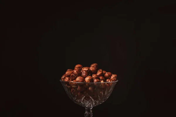 Close up view of shelled hazelnuts in glassware on black backdrop — Stock Photo