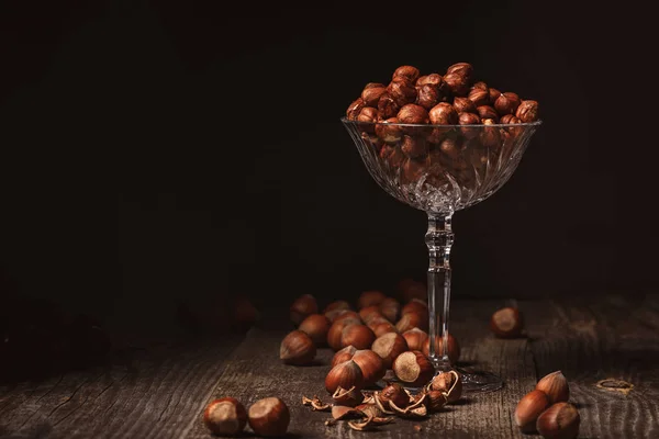 Close up view of shelled hazelnuts in glassware on wooden surface on black background — Stock Photo