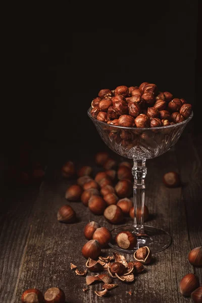 Close up view of shelled hazelnuts in glassware on wooden surface on black background — Stock Photo