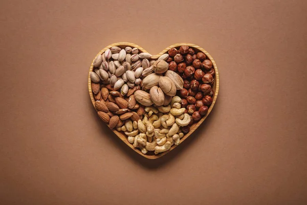Top view of assortment of various nuts in heart shaped box on brown backdrop — Stock Photo