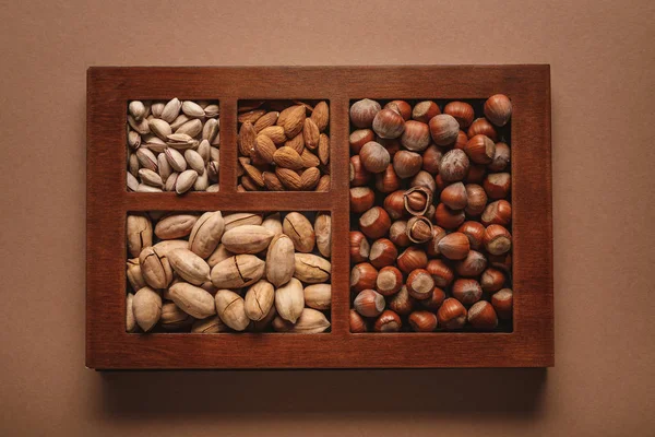 Top view of assortment of various nuts in box on brown background — Stock Photo