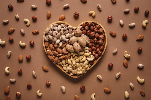 Flat lay with heart shaped box with different nuts assortment on brown tabletop — Stock Photo