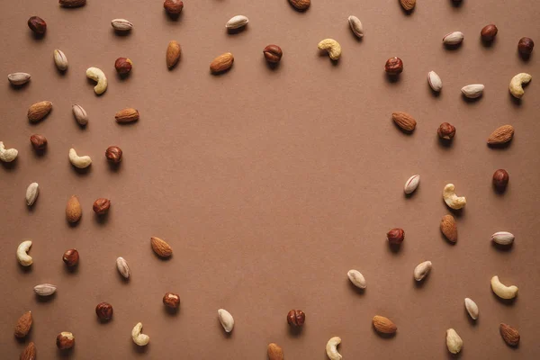 Повна рамка з різних горіхів, розташованих на коричневому тлі з порожнім простором посередині — стокове фото