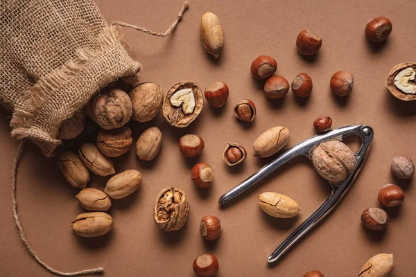 Flat lay with nuts, nutcracker and sack on brown backdrop — Stock Photo