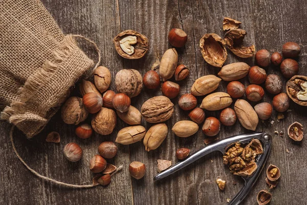 Posa piatta con noci, schiaccianoci e sacco su tavolo in legno — Foto stock