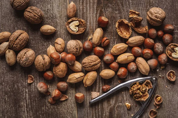 Top view of various nuts and nutcracker on wooden surface — Stock Photo