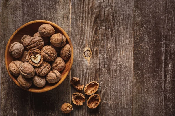 Top view of walnuts in bowl on wooden tabletop with husk — Stock Photo