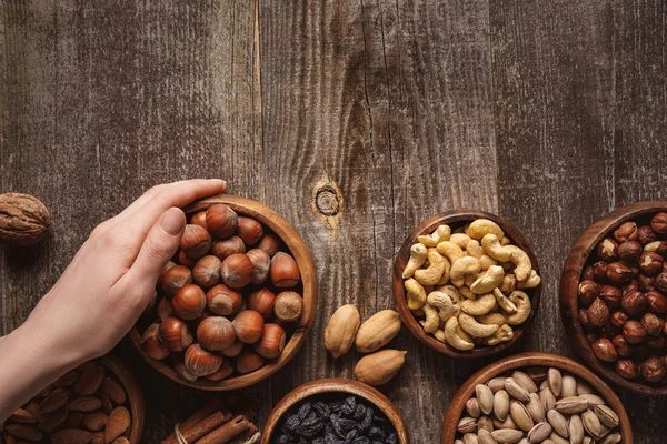 Partial view of woman holding bowl with hazelnuts on wooden tabletop with different nuts around — Stock Photo