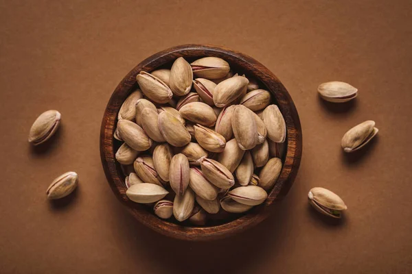 Top view of pistachio nuts in wooden bowl on brown backdrop — Stock Photo
