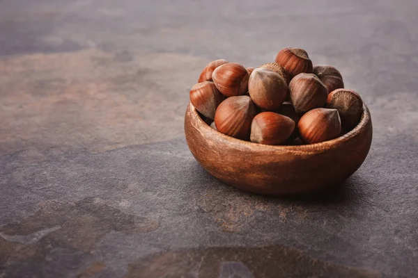 Close up view of shelled hazelnuts in wooden bowl on grey tabletop — Stock Photo