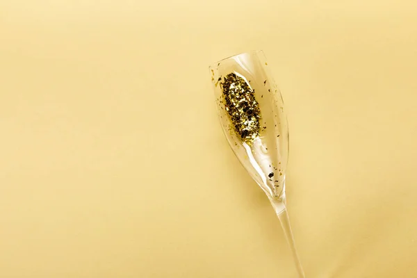 Close-up view of champagne glass with golden confetti on beige background — Stock Photo