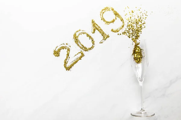 Números 2019 y copa de champán con confeti dorado sobre fondo blanco - foto de stock