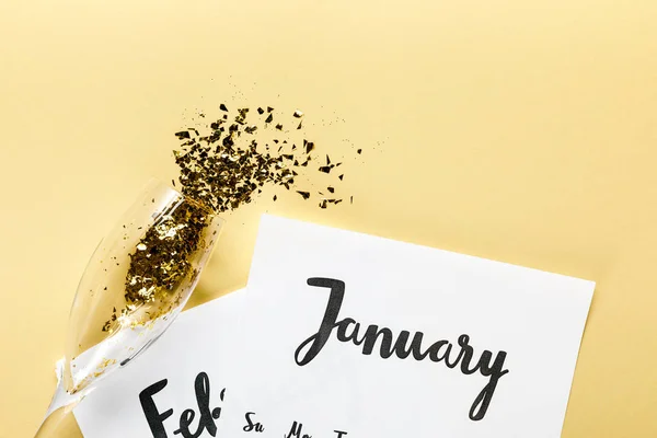 Verre à champagne avec confettis dorés, papiers avec calendrier janvier et février sur fond beige — Photo de stock