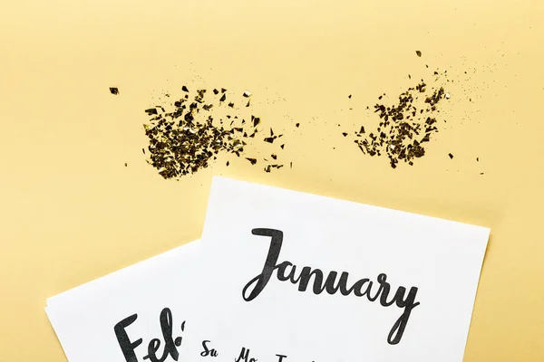 Goldenes Konfetti mit Januar- und Februar-Kalender auf beigem Hintergrund — Stockfoto
