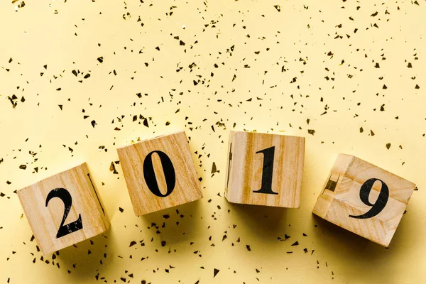 Top view of wooden cubes with 2019 numbers and golden confetti on beige — Stock Photo