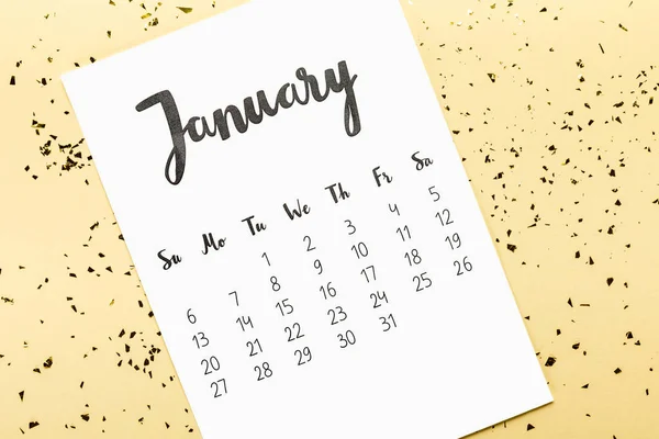 Vista superior del calendario de enero y confeti dorado en beige - foto de stock