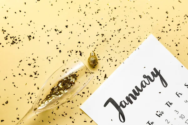 Vue du haut du calendrier de janvier, boule de Noël et verre avec confettis dorés sur beige — Photo de stock