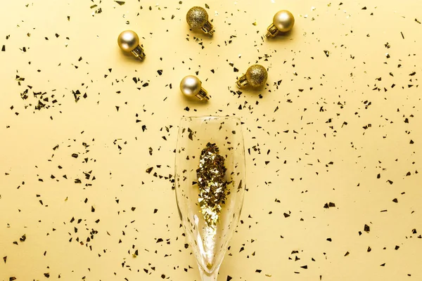 Vista superior de la copa de vino, adornos de Navidad y confeti dorado festivo sobre fondo beige - foto de stock
