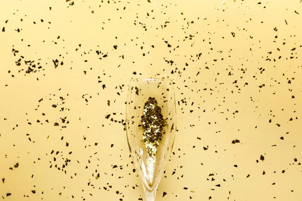 Champagne glass and festive golden confetti on beige background — Stock Photo
