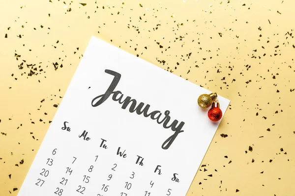 Vista superior del calendario de enero y adornos navideños con confeti dorado sobre fondo beige - foto de stock