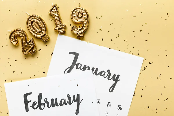 Vista superior del calendario de invierno, velas 2019 y confeti dorado sobre fondo beige - foto de stock