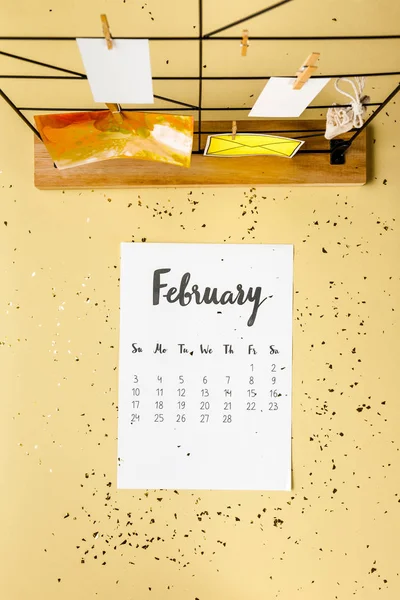 Vista dall'alto del calendario febbraio con coriandoli dorati e cartoline con mollette su beige — Foto stock