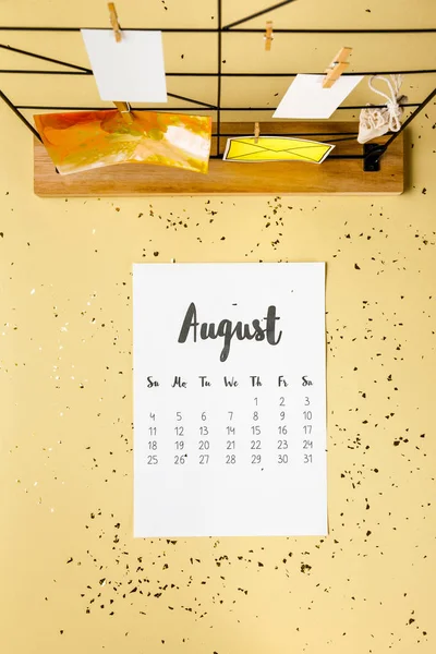 Vista superior del calendario de agosto con confeti dorado y tarjetas con pinzas de ropa en beige - foto de stock