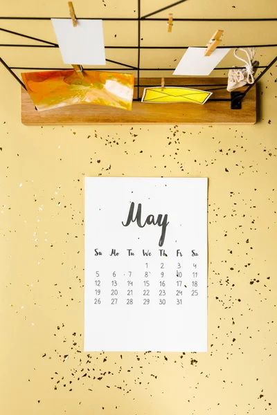 Vista superior do calendário de maio com confete dourado e cartões com espinhas de roupa em bege — Fotografia de Stock
