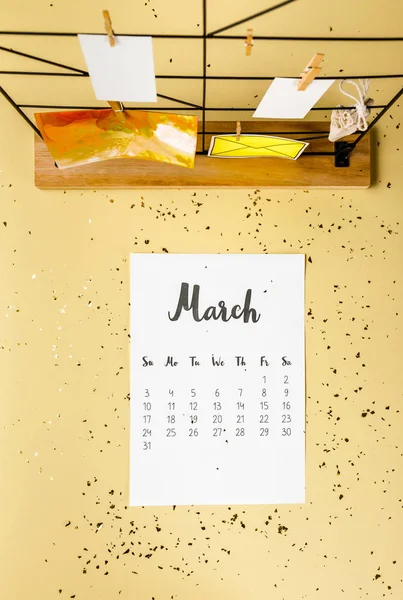 Vista superior del calendario de marzo con confeti dorado y tarjetas con pinzas de ropa en beige - foto de stock
