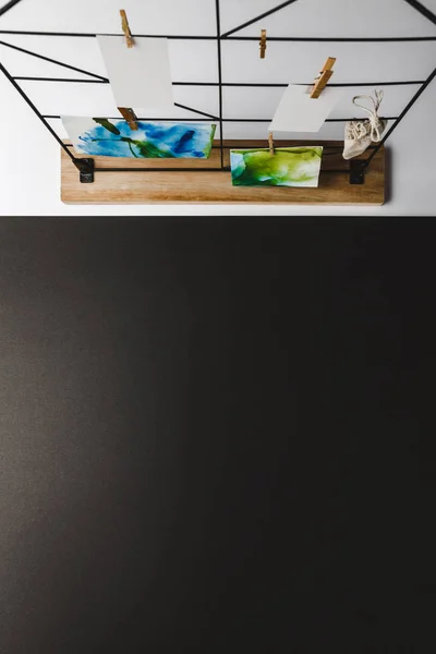 Vista superior de hermosas pinturas abstractas y tarjetas en blanco colgando de pinzas de ropa, fondo negro - foto de stock