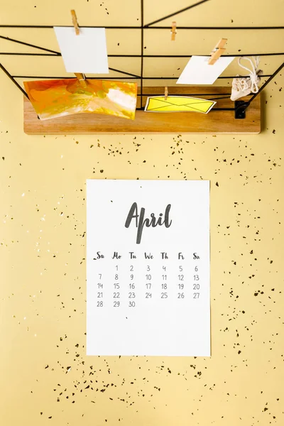 Vista superior del calendario de abril con confeti dorado y tarjetas con pinzas de ropa en beige - foto de stock